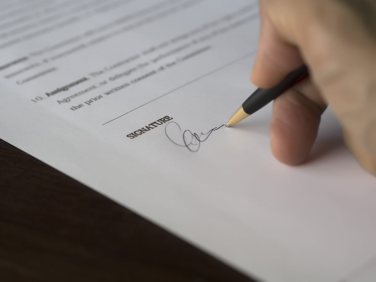 Gros plan d'une main signant un document officiel sur un bureau en bois